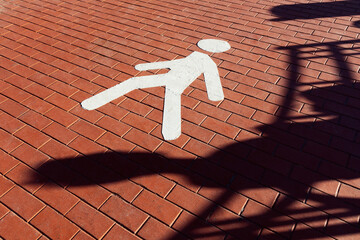 Sign of pedestrian zone in form of white human figure markings on red paving stones and shadow of sitting person