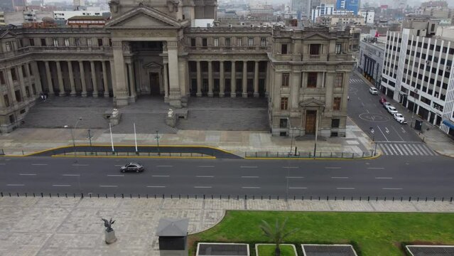 Drone footage of Peru's supreme court called Palace of Justice in the capital of Lima. Drone flies left to right while tilting camera up. a few cars can be seen driving on street. Peruvian flag on top