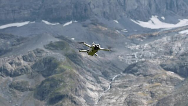 Drone dji mini 3 pro hovering in the air and it does not move in front of a rocky mountain in the swiss alps