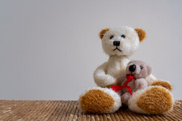 Closeup of white and brown teddy bear with cute bear cub wearing red ribbon sitting in lap isolated on light background