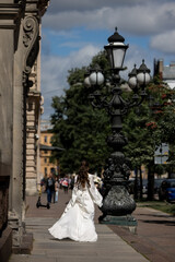 Bride in a white dress runs along the old street Back view