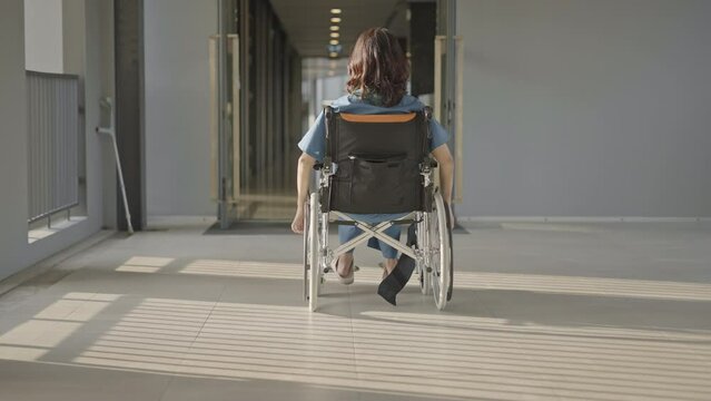 Rear view of a woman in wheelchair in hospital hallway