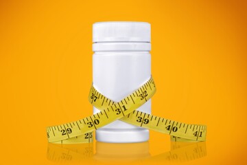 A jar with tablets in capsules stands in front of a measuring tape. The concept of weight loss, fat...