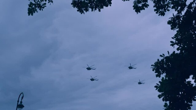 The formation of helicopters flying over the city. View of helicopters in the air from below from the ground. Silhouettes of flying helicopters against the sky.