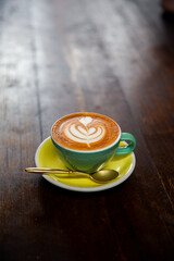 green mug of cappuccino with latte art on wooden background.