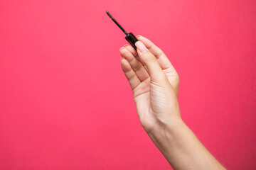 Close up of woman's hand holding an eyebrows brush mascara on pink background