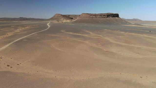 Bird's eye view of Gara Medouar rock formation and tire marks on desert sand in Morocco. Aerial drone pov