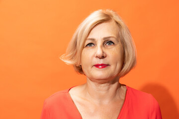 Half-length portrait of beautiful middle age woman with blond hair posing isolated on orange color background. Concept of emotions, facial expressions