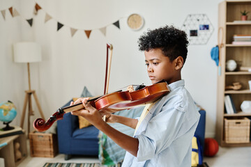 African little boy practicing and learning to play violin during home lesson