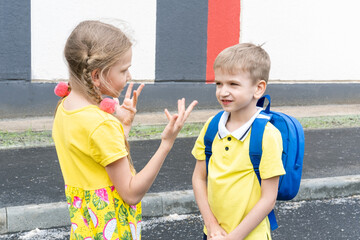 Back to school. The older sister tells gestures to the younger brother with a school backpack....
