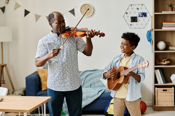 African little boy playing guitar with his teacher playing violin during home lesson