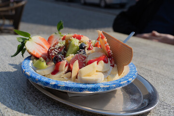 Bowl with delicious ice cream and lots of fruits on a wooden table of an ice cream shop