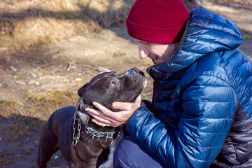 Close-up portrait of a man and a dog, a black pit bull faithfully looks into the eyes of his owner, love for animals	