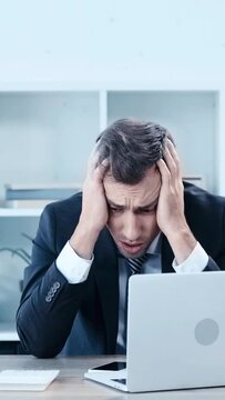 vertical video of upset businessman throwing papers with and covering head with hands while sitting at workplace