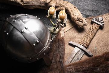 Viking sword, helmet and animal fur skin on the old wooden table close up.