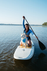 Young Woman with Dreads Paddleboarding with Her Pet on the City Lake, Snow-White Japanese Spitz Dog Standing on Sup Board