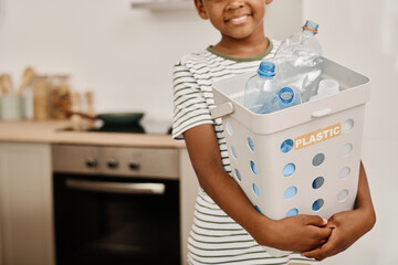 Portrait of African boy holding container with plastic bottles and smiling at camera standing in...