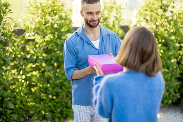 Man gives a gift in pink box to his woman, celebrating anniversary in the yard of their house. Celebration of thanksgiving day, valentine or birthday concept