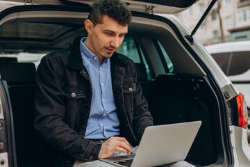 Man sitting in trunk of his car and working on computer