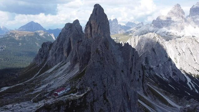 A stunning drone shot of a lonely house (named Rifugio Fratelli Fonda Savio) located in the middle of the mountains and rock formations of the Dolomites in South Tyrol in Italy