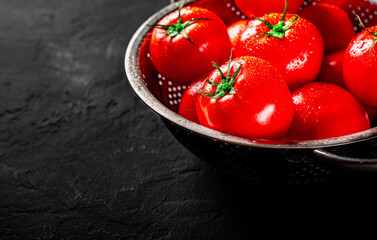 raw whole washed tomatoes in a colander on Dark grey black slate background with copy space - obrazy, fototapety, plakaty