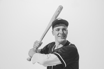 Black and white portrait of smiling young man, baseball player in uniform with bat preparing to hit...