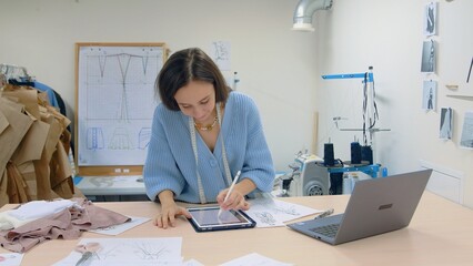 Obraz premium 4K. A young woman working in a clothing store. A fashion designer makes sketches on a tablet.
