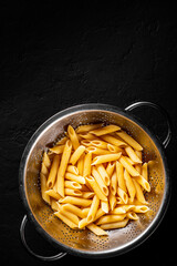 Fototapeta cooked Penne rigate pasta in stainless steel colander on Dark grey black slate background with copy space. top view obraz