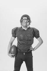Portrait of young smiling man, american football player posing in full equipment with ball. Black and white photography