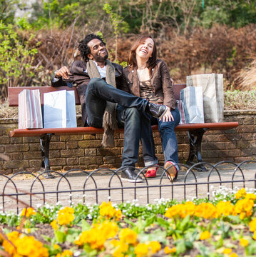 London shoppers; Park Life. A young mixed race couple take a rest in a park after a day out shopping. From a series of images.
