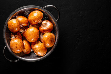 Fototapeta Fresh raw mushrooms champignons in stainless steel colander on Dark grey black slate background with copy space. top view obraz