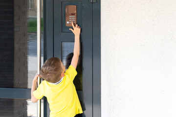 A little boy reaches for the bell to ring the doorbell, a view from the back, copy space. A child standing near the front door of the house. The child returns home.