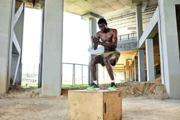 Obraz na płótnie Canvas Muscular black athlete jumping on wooden box. Urban background.