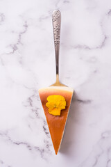 Sweet cheese cake with yellow flower on a cake server. Marble background. Mouthwatering dessert....