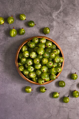 Ripe green gooseberries in a bowl on a gray concrete background. Flat lay composition, copy space. Harvest concept. Vegetarian food. Vertical photo 