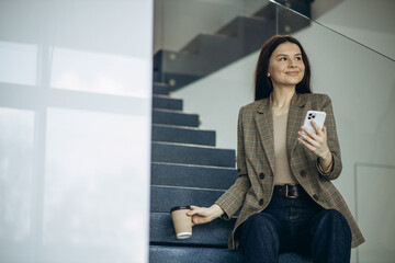 Woman sitting on stairs drinking coffee and using phone