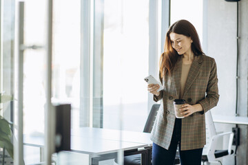 Business woman drinking coffee and using phone in office