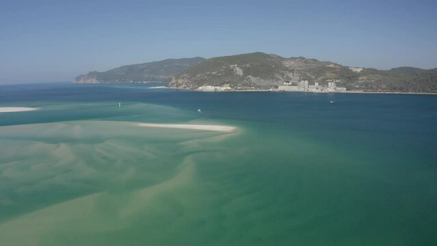 Aerial panning shot showing turquoise ocean and Troia Island during sunny day in Portugal