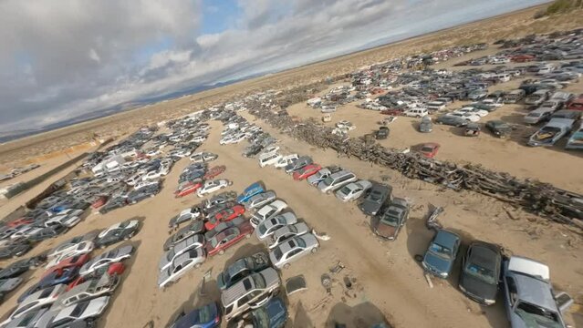 FPV aerials diving from high above and fast flying over and through a vast automotive junkyard in the California desert near Lancaster