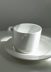 a white porcelain cup stands on a saucer in the morning sun