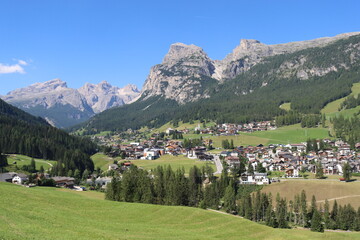 Coravara, Italy-July 16, 2022: The italian Dolomites behind the small village of Corvara in summer days with beaitiful blue sky in the background. Green nature in the middle of the rocks.