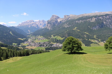 Fototapeta premium Coravara, Italy-July 16, 2022: The italian Dolomites behind the small village of Corvara in summer days with beaitiful blue sky in the background. Green nature in the middle of the rocks.
