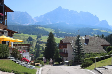 Fototapeta premium Coravara, Italy-July 16, 2022: The italian Dolomites behind the small village of Corvara in summer days with beaitiful blue sky in the background. Green nature in the middle of the rocks.
