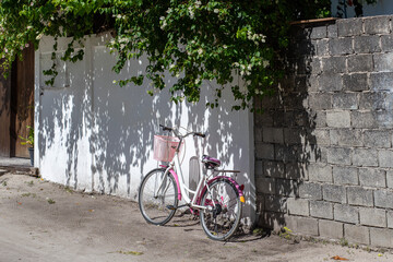 A white and pink retro bicycle with a basket stands near a white wall on the street