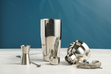 Bartender equipment - stainless steel silver colored cocktail shaker, hawthorne strainer, pourers, bar spoon, muddler , in a bamboos stand on white table on blue background