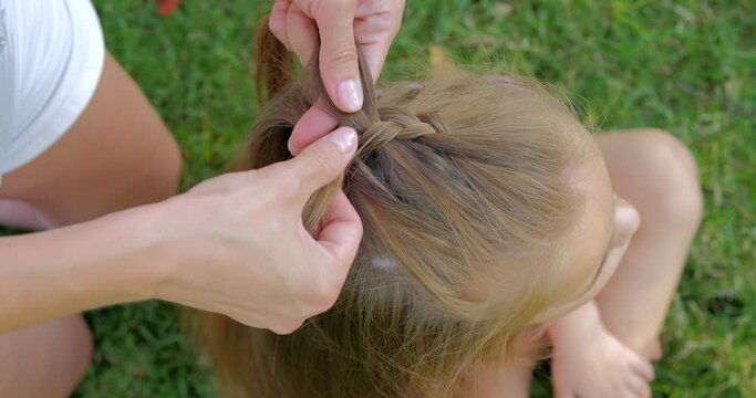 Mother making hairstyle french braid her daughter outdoor