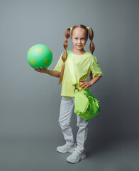 a small young girl with a green sword in her hand smiles at the camera, isolated on a gray background. a little athlete with a ball. children's sports.