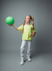 a small young girl with a green sword in her hand smiles at the camera, isolated on a gray background. a little athlete with a ball. children's sports.