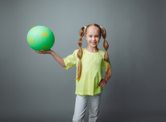 a small young girl with a green sword in her hand smiles at the camera, isolated on a gray background. a little athlete with a ball. children's sports.