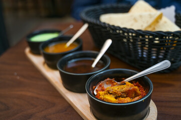 Indian dip, relish, chutney and sauce served in small black bowls with crispy papadam bread on a dark wooden table, copy space, selected focus